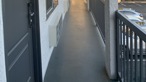 Ein Korridor mit einer Tür, auf der „205“ steht, einem Geländer und Blick auf Bäume sowie einen Parkplatz.