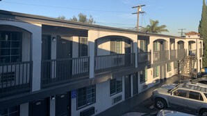 Ein mehrstöckiges Motel mit einer Reihe von Zimmern im Erdgeschoss, einem überdachten Parkbereich und einer Treppe zu den oberen Stockwerken.