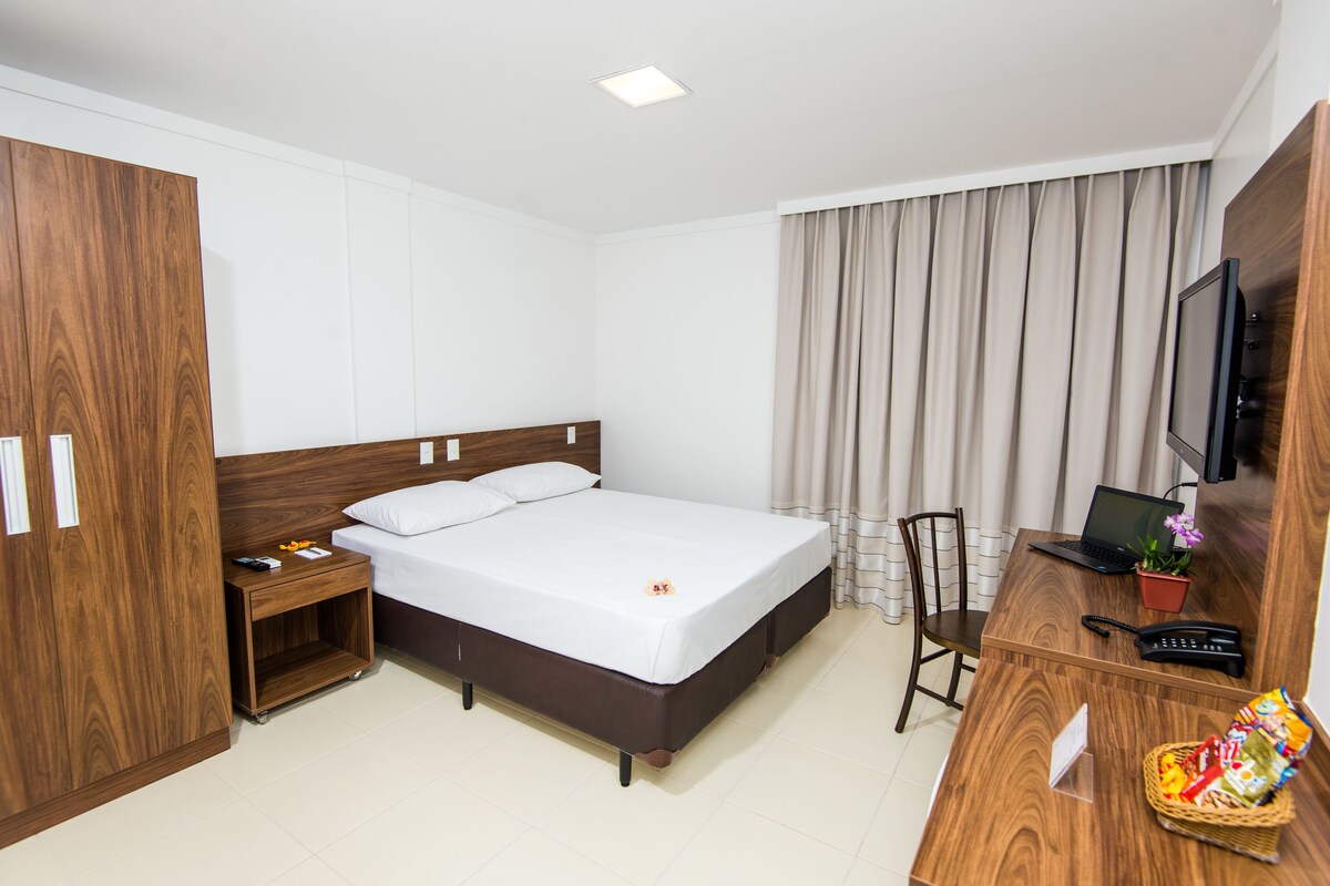 Une chambre d’hôtel comprenant un lit, un bureau avec un ordinateur portable, une télévision et une armoire.