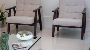Dos sillones con tela clara y patas de madera oscura, sobre un suelo blanco brillante.