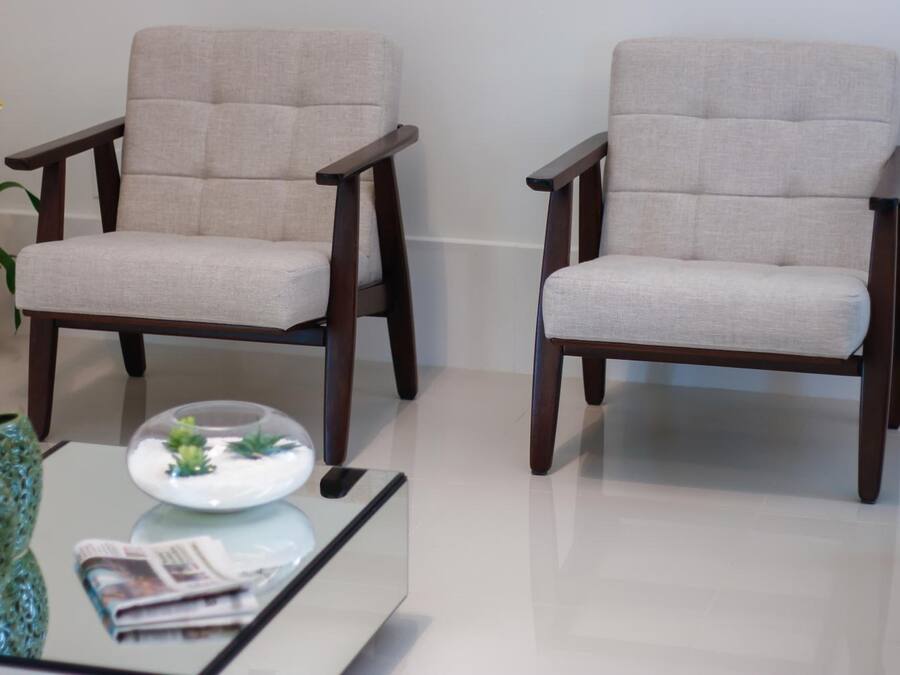 Two armchairs with a light fabric and dark wooden legs, placed on a glossy white floor.