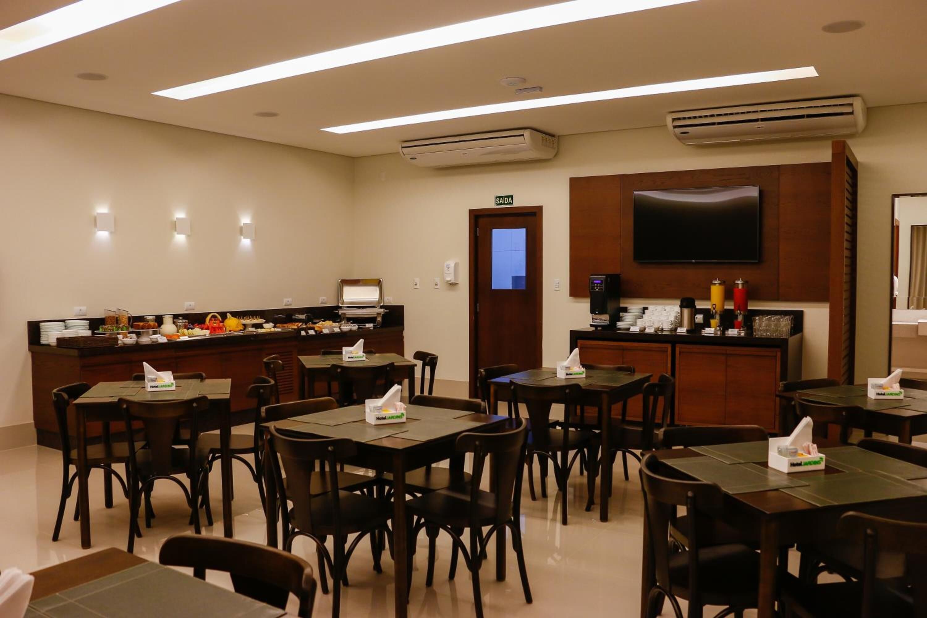 A hotel dining area with tables, chairs, a buffet counter, a television, and an exit door.