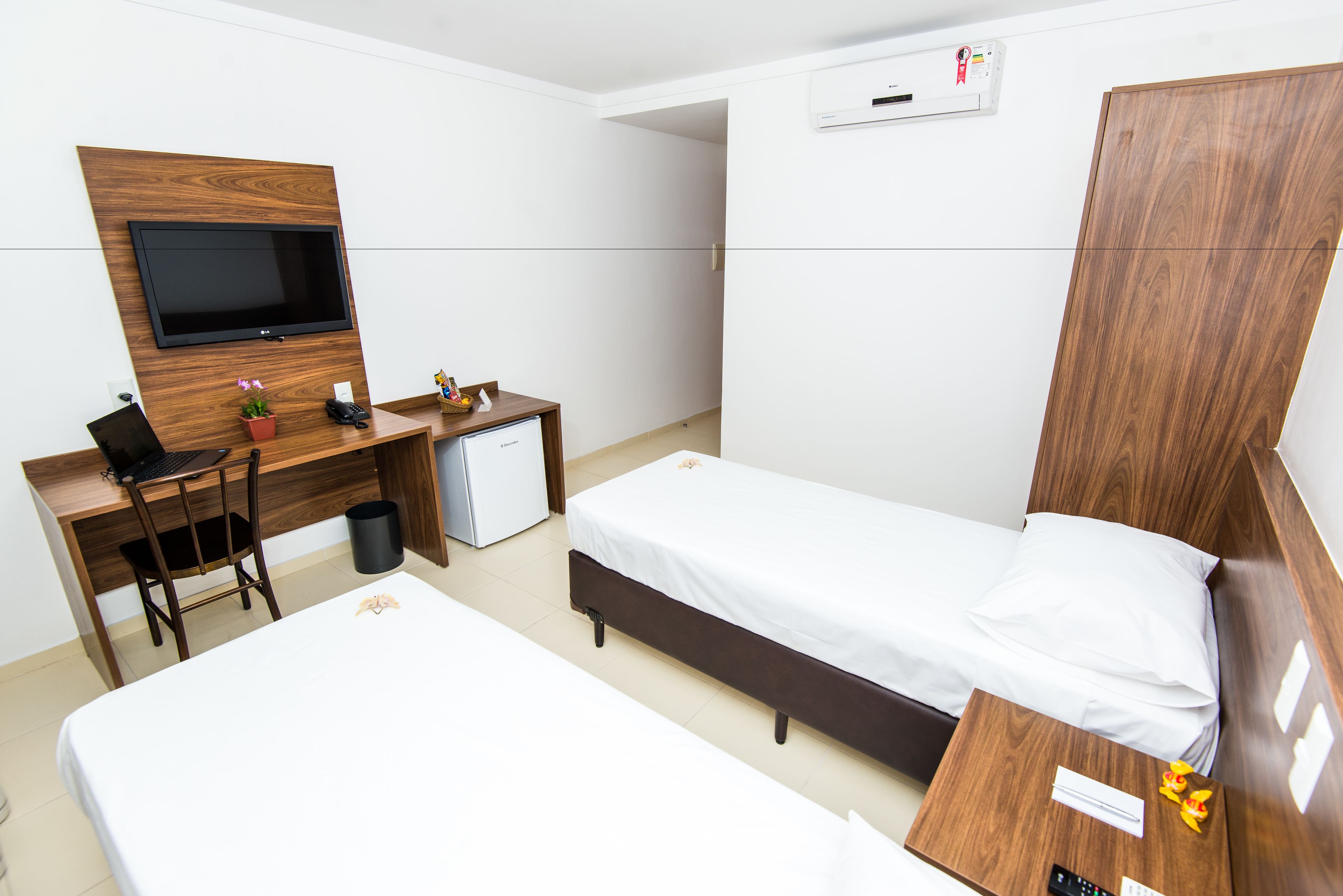 Una habitación de hotel con una cama, un escritorio con computadora, televisor y armario.
