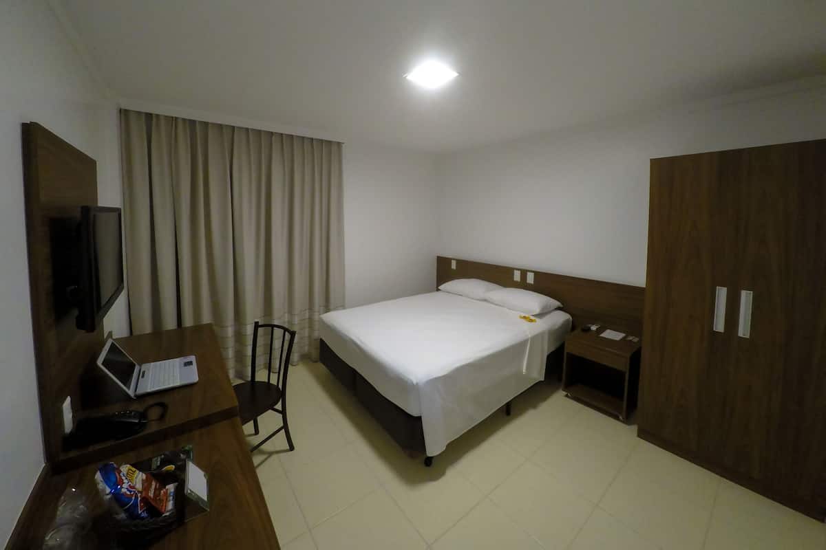 Una habitación de hotel con una cama, un escritorio con una computadora portátil, una silla, un televisor y un armario.