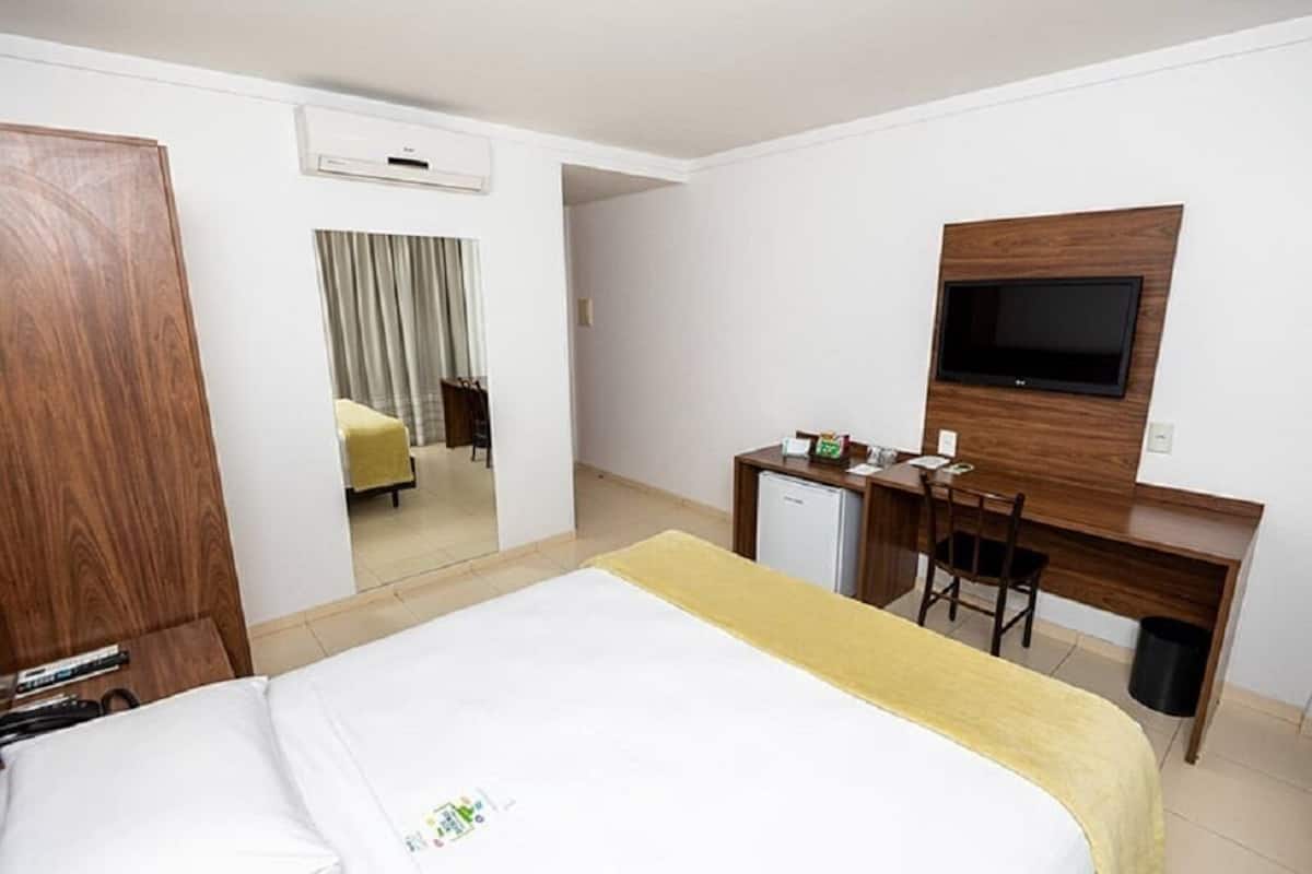 Una habitación de hotel con una cama, un escritorio, un televisor y un espejo.