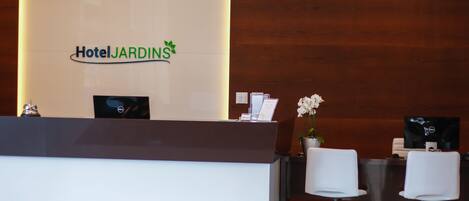 Una recepción con un cartel que dice "HotelJARDINS" y un diseño moderno con un fondo de pared de madera.