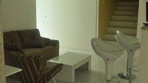 A modern living room with a striped sofa, a white coffee table, and two bar stools. - Pousada N S Fátima (Fortaleza)