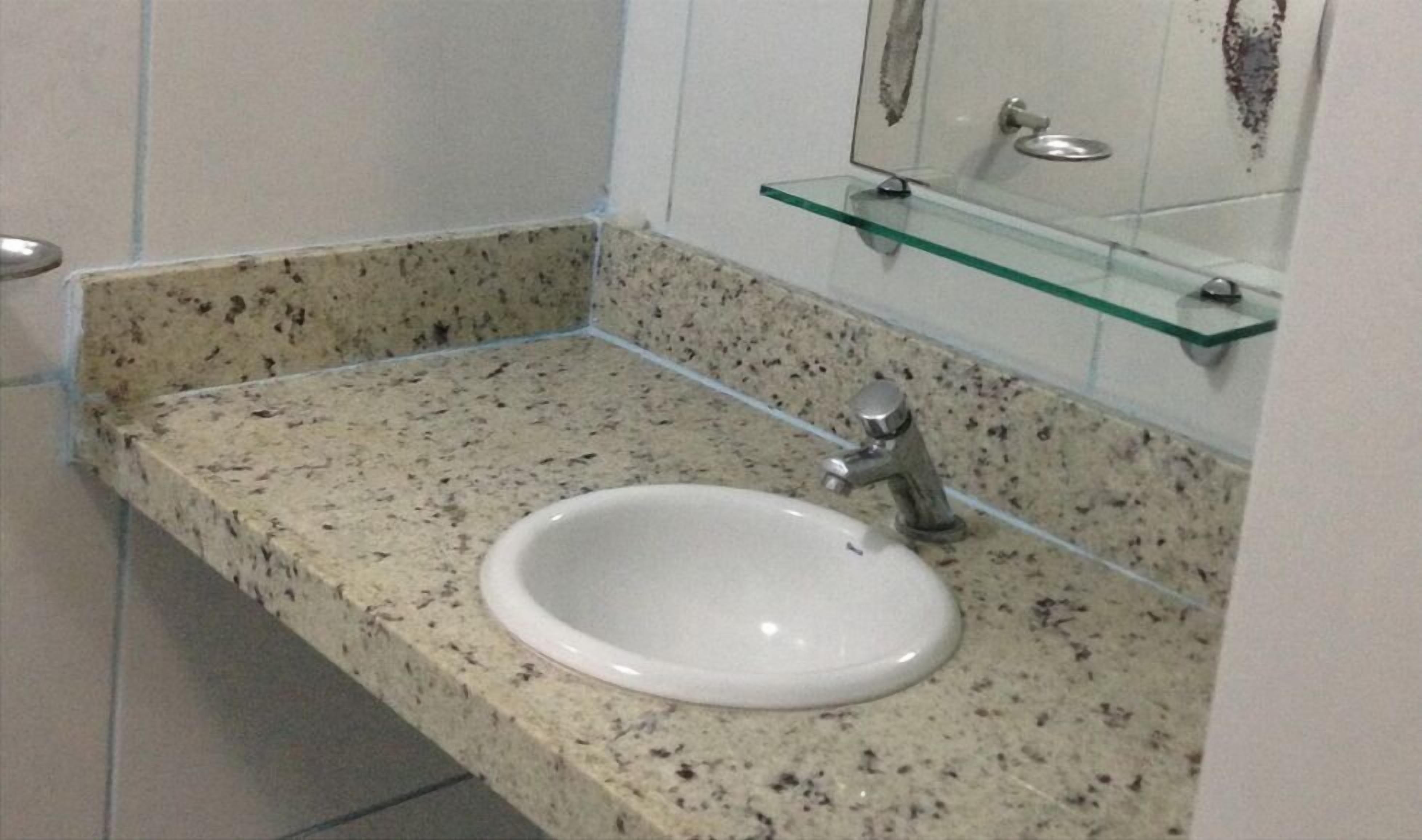 A bathroom with a granite countertop, a white sink, and a glass shelf above it.