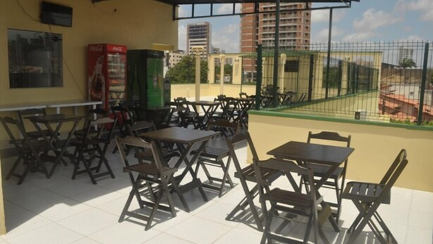 An outdoor seating area with tables and chairs, a Coca-Cola refrigerator, and a view of buildings in the background. - Pousada N S Fátima (Fortaleza)