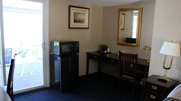 Habitación de hotel con escritorio, una silla, cama, televisor, microondas, lámpara y ventana con vistas al exterior.