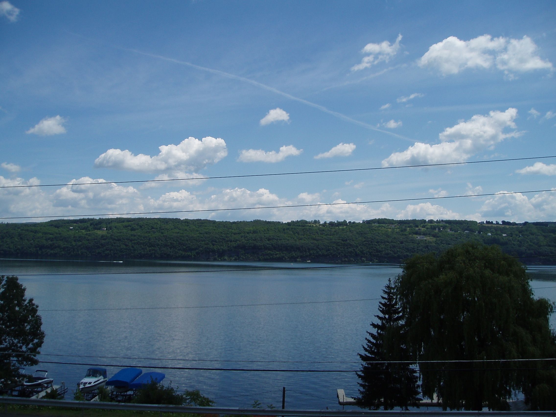 Une vue d’un lac, avec une colline boisée en arrière-plan et une ligne électrique traversant le ciel.
