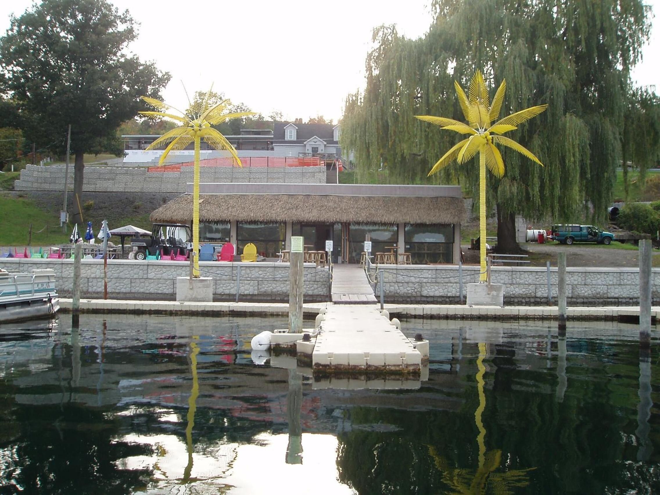 Una zona frente al agua con un restaurante, un muelle y esculturas de palmeras.