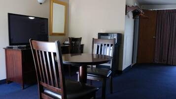 Habitación de hotel con una mesa redonda de comedor, cuatro sillas de madera, un televisor de pantalla plana, un espejo y un perchero.