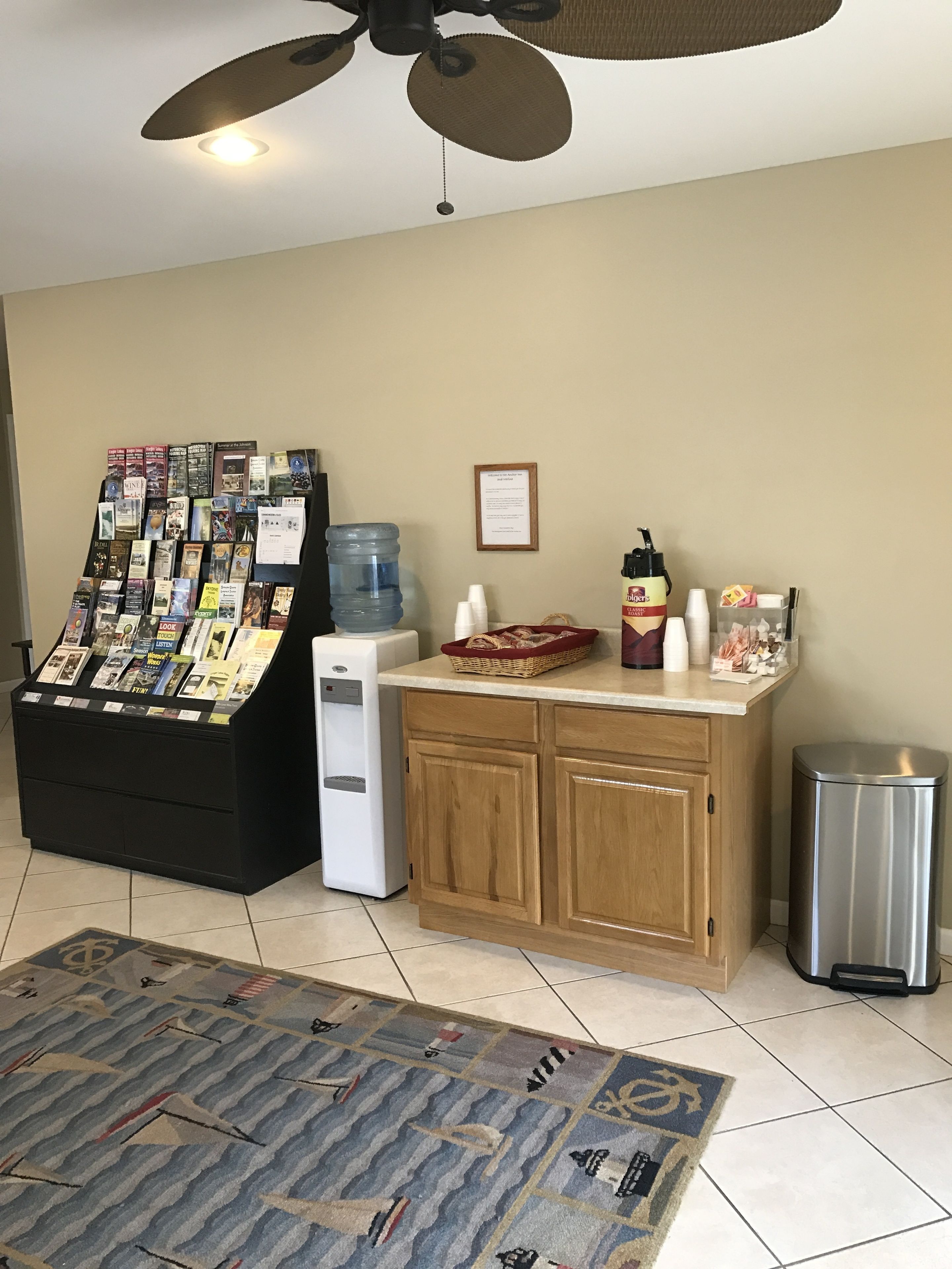 A room with a book display, a water dispenser, a waste bin, and a ceiling fan.
