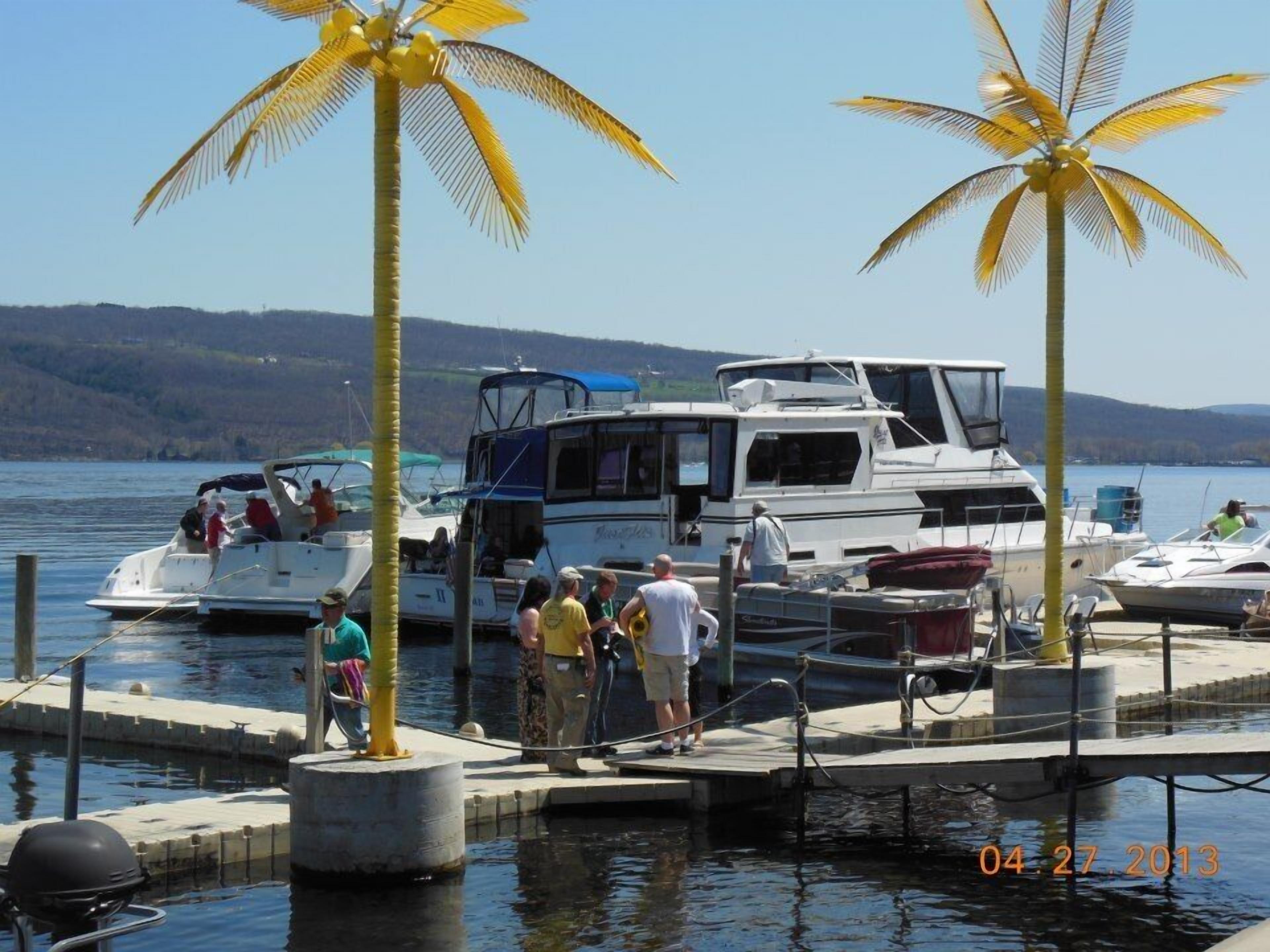 A marina with boats docked, a dock with people, and palm trees.