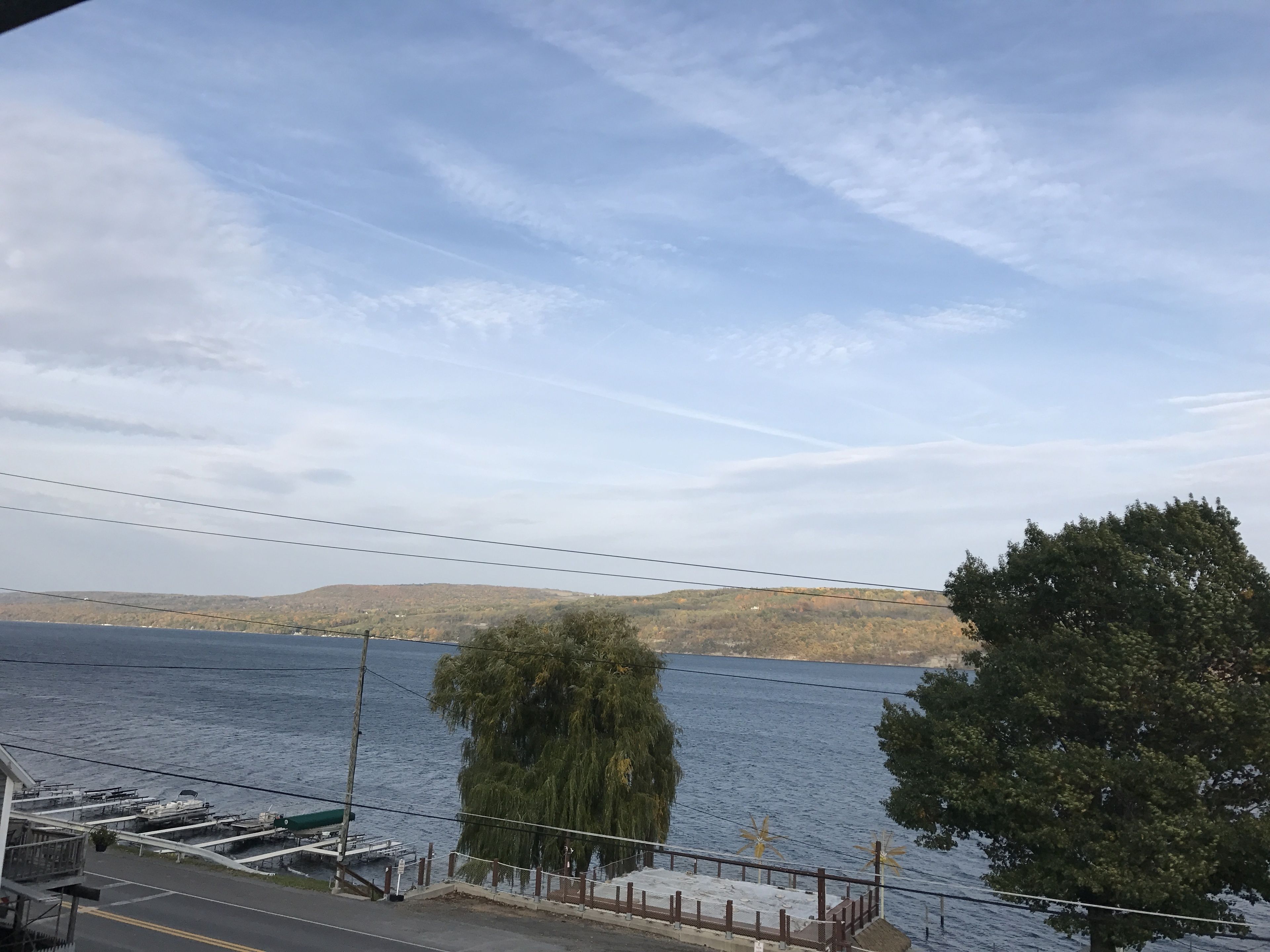 A waterfront view with docked boats, a road with a fence, and a hilly landscape in the background.