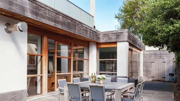 Una veranda esterna con tavolo e sedie, ampie finestre e un terrazza in legno.