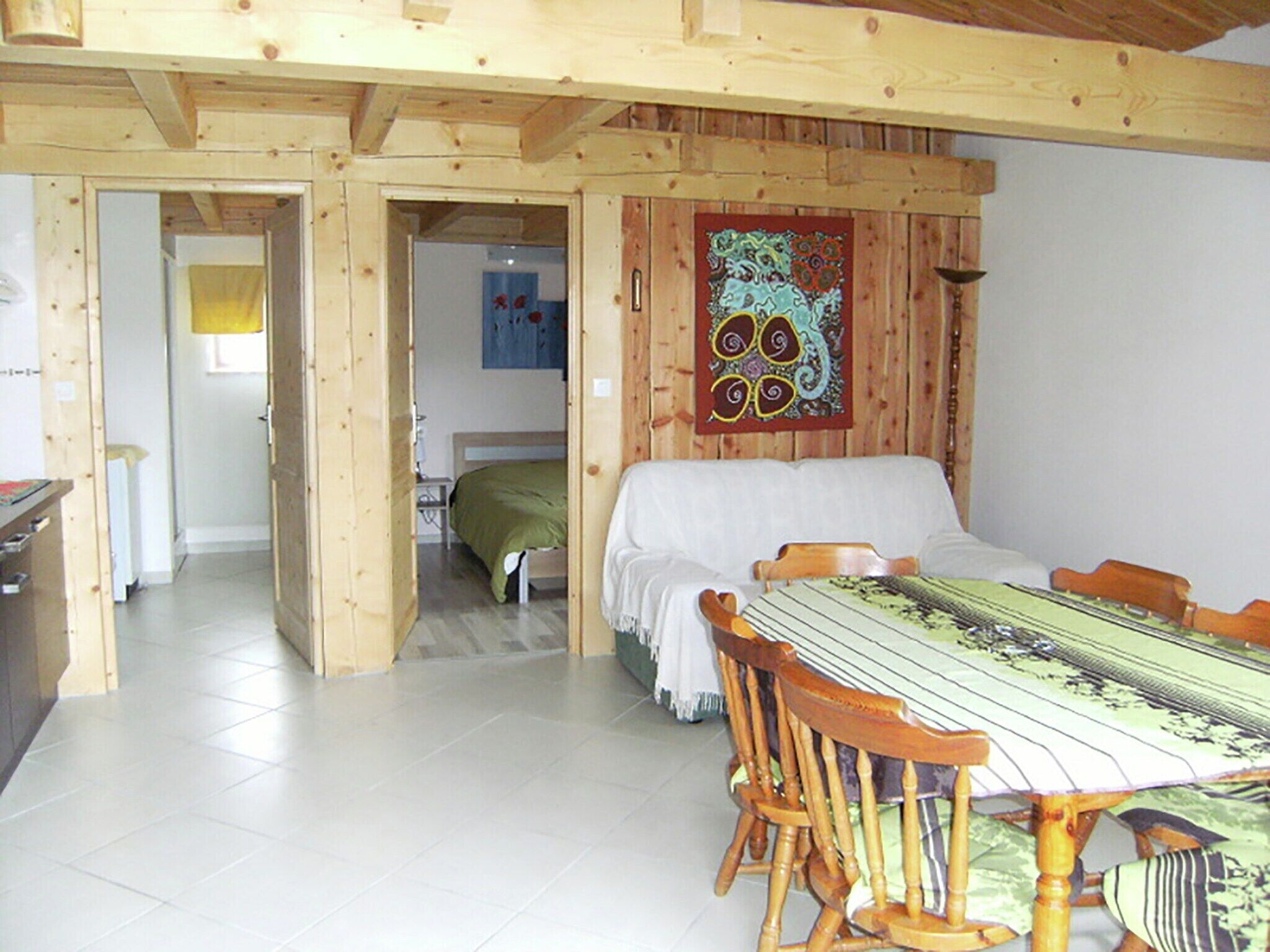 Un intérieur en bois avec une table et des chaises, un lit à l’arrière-plan et une tapisserie colorée au mur.
