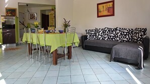 Een eethoek met een tafel voor vier personen, een bank met gestreepte kussens, en een keuken op de achtergrond.