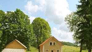 Landlig omgivelser med et gult hus, en bygning i sten og et hegn med en bil foran.