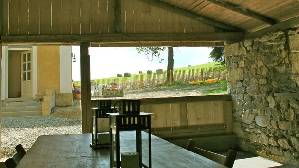 En udendørs terrasse med stenvægge, et træbord og stole.