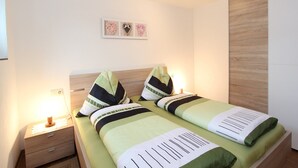 A neatly made bed with green bedding, a wooden nightstand with a lamp, and a wall-mounted picture above the bed. - Apartment in Stuhlfelden near Ski Lift (Stuhlfelden)