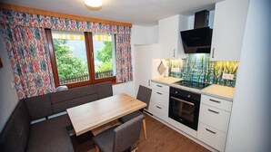 A compact kitchen with a dining area, featuring a built-in stove, white cabinets, and a window with patterned curtains. - Apartment in Stuhlfelden near Ski Lift (Stuhlfelden)