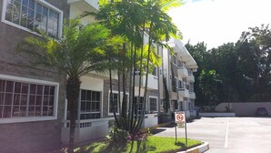 A multi-story building with balconies, surrounded by palm trees and a parking area.