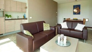 Ein modernes Wohnzimmer mit einer braunen Ledersofa, einem Esstisch mit Kerzen und einer Küchenzeile mit hellen Holzschränken.