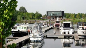 Ein Hafen mit mehreren dort liegenden Booten, ein modernes Gebäude im Hintergrund und üppiges Grün in der Umgebung.