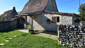 A stone house with a tiled roof, a small porch with chairs, and a stone wall. - Holiday Home in Gramat with Private Pool (Gramat)