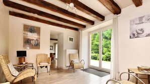 A spacious room with wooden floors, wicker furniture, and a large sliding glass door leading to a garden. - Fine group house with sauna garden (Chiny)