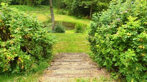 A wooden pathway leading through a lush garden with dense foliage on either side. - Fine group house with sauna garden (Chiny)