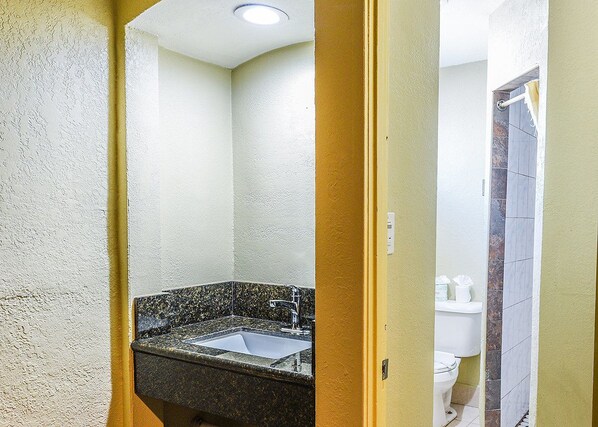 Un baño con lavamanos de granito, paredes blancas y un marco de puerta amarillo.