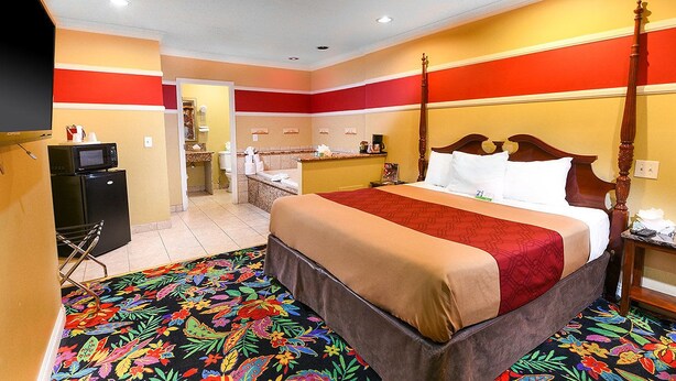 A hotel room with a four-poster bed, a microwave, a refrigerator, a bathroom, and a colorful carpet. - Pacifica Motel (Long Beach)