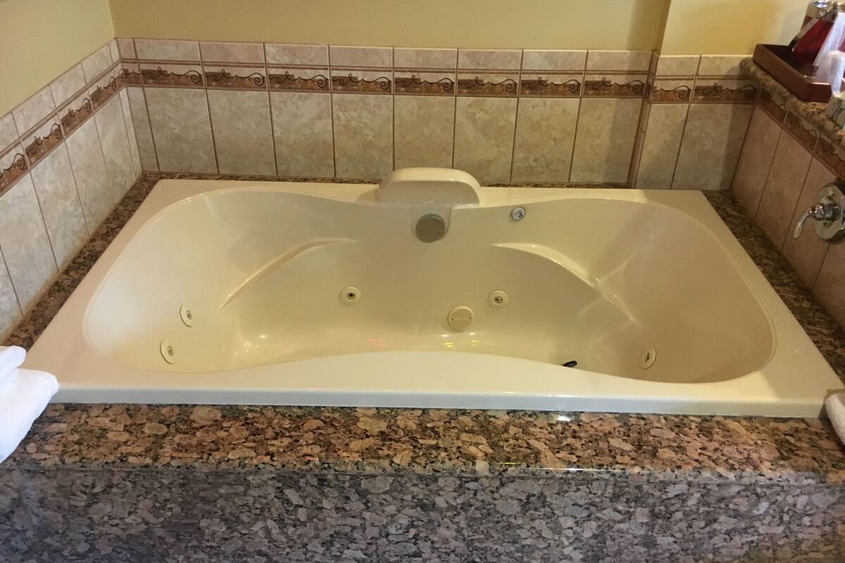 Une salle de bain dotée d’une grande baignoire, d’un comptoir en granit et d’une bordure décorative en carreaux.