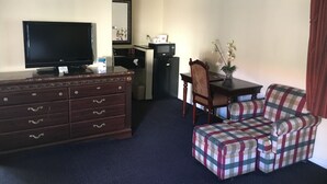 A hotel room with a flat-screen TV, a wooden dresser, a dining table with chairs, and a checkered sofa. - Pacifica Motel (Long Beach)