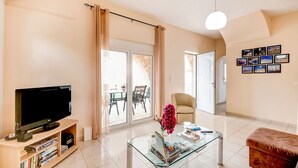 Uma sala de estar com televisão de tela plana, uma mesa de centro de vidro, um sofá e um espaço de jantar com mesa e cadeiras.