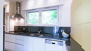 A modern kitchen with white cabinets, a black countertop, a Bosch dishwasher, and a window with a view of greenery. - Oostduinkerke Forestside Villa (Oostduinkerke)
