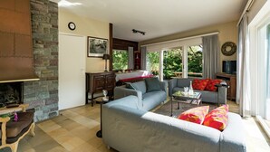 A spacious living area with a stone fireplace, a sofa set, a dining table, and a view of the outdoors. - Oostduinkerke Forestside Villa (Oostduinkerke)