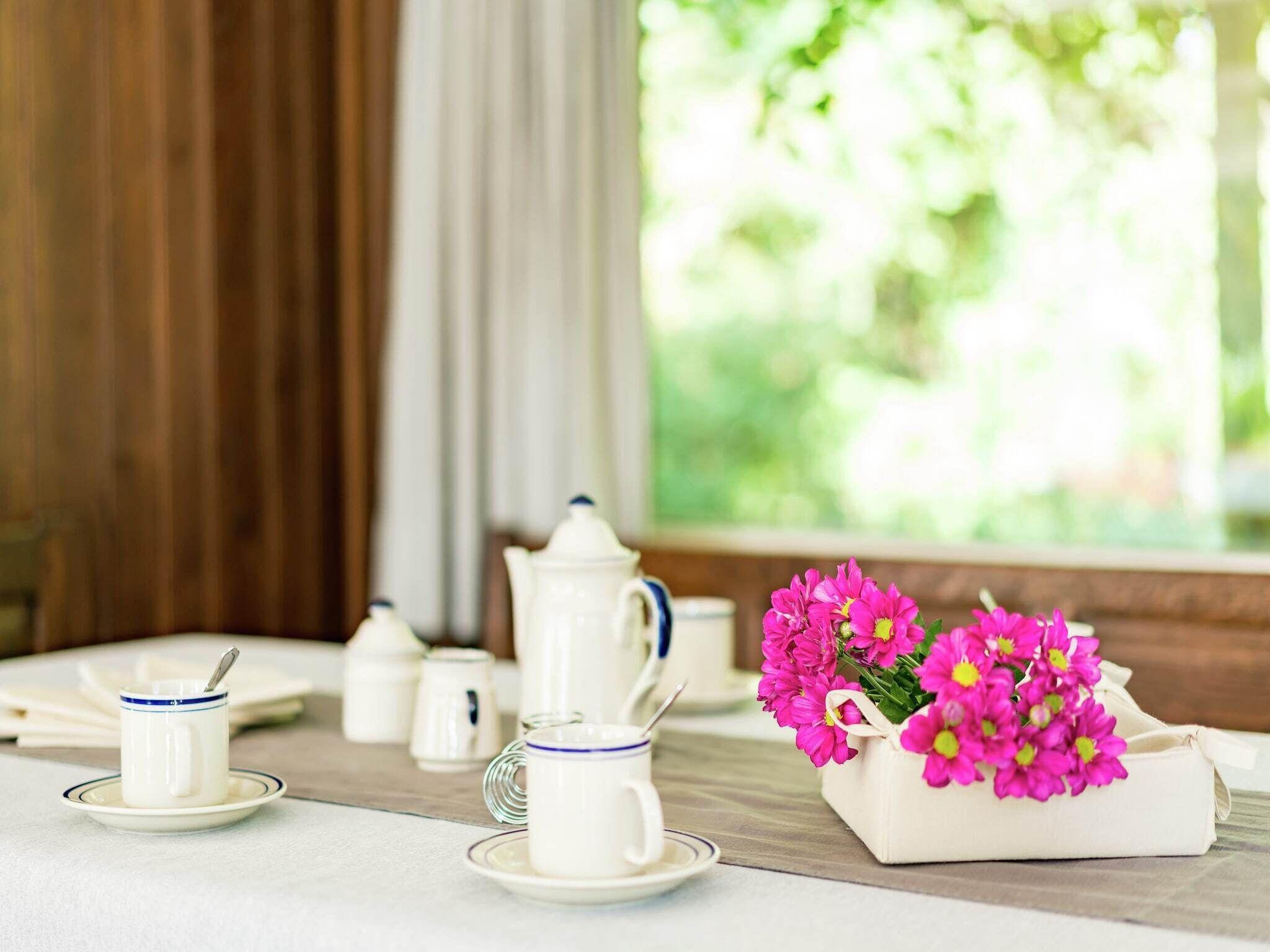 Ett prydligt dukat bord med vita tekoppar, en tekanna och en vas med rosa blommor.