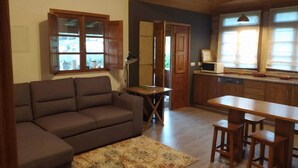 A living room with a sofa, a coffee table, and a patterned rug. There is a kitchen area with a microwave and a window with blinds. - Countryside Cottage with Private Terrace (Gondufe, Ponte de Lima)