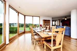 Enjoy meals in this serene dining area with a large table and comfortable chairs, surrounded by a lush landscape view.