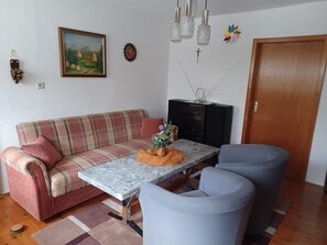 Una sala de estar con sofá, una mesa de centro, dos sillones, televisor y una puerta.