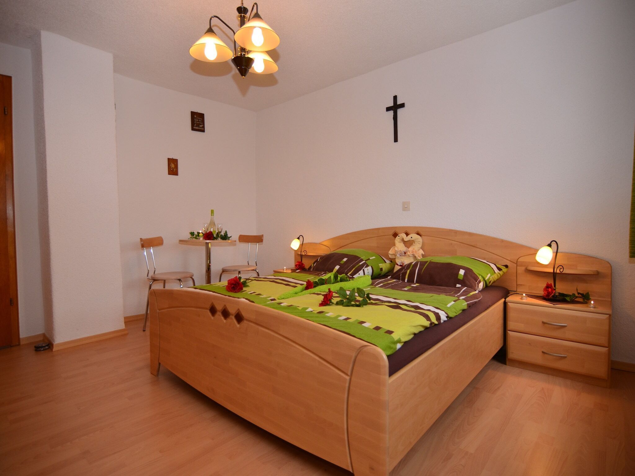 A bedroom with a wooden bed, bedside tables, a cross on the wall, and a chandelier.