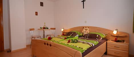 A bedroom with a wooden bed, bedside tables, a cross on the wall, and a chandelier.