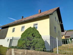 Un edificio de dos plantas con fachada amarilla, techo de tejas rojas y una valla metálica.
