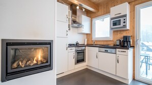 Une cuisine moderne dotée d’une cheminée intégrée, de meubles blancs, d’appareils électroménagers en acier inoxydable et d’une grande fenêtre.