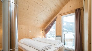 Une chambre à coucher dans une cabane en bois, avec un lit, une fenêtre avec des rideaux et une vue sur un paysage enneigé.