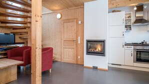 Un intérieur moderne avec une cheminée, des poutres en bois, une cuisine et un fauteuil rouge.